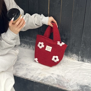 Detail of red plush handbag with white floral accents and woven brand label