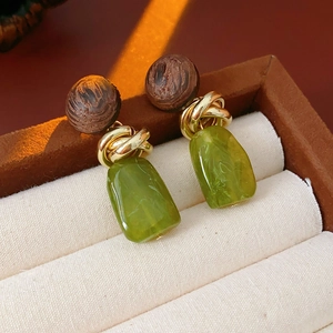 Close-up of vintage geometric earrings with wood beads and green resin pendants on beige fabric
