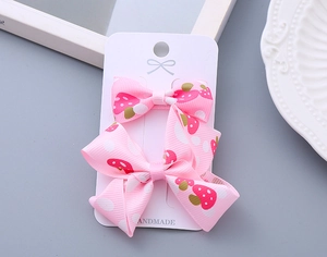 Detail of two pink strawberry and polka dot handmade bow hair clips on display card