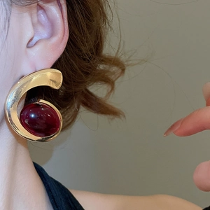 Close-up of model wearing gold C-shaped earrings with large deep red oval gemstones