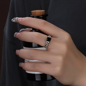 Detail of a silver chain ring with a square black gemstone worn by a model