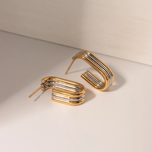 Close-up of modern two-tone rectangular C-shaped earrings in polished gold and silver metal