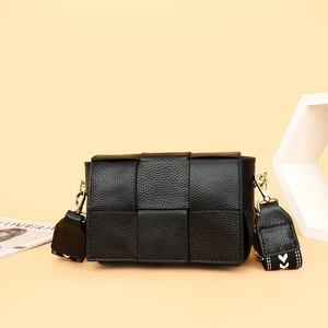 Black woven leather crossbody bag with geometric strap on a cream minimalist background