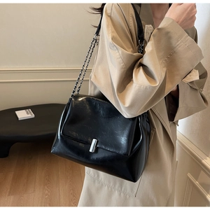 Detail of black glossy shoulder bag with silver metallic buckle and chain strap