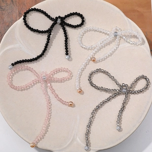 Handmade beaded crystal bow charms in black, pink, and clear colors on ceramic tray