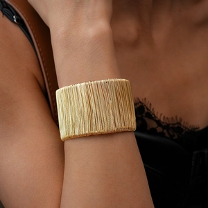 Detailed view of a wide gold-wrapped wire bracelet showing intricate metal texture on wrist