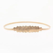 Detailed close-up of golden metal leaf belt buckle with textured finish on white background