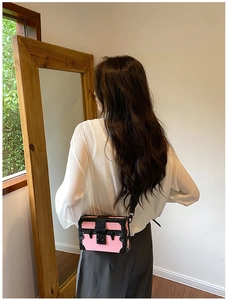 Pink trunk bag with black rivet trim and adjustable shoulder strap shown on a model