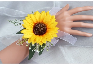Detail of sunflower wrist corsage with yellow petals, green leaves and white organza ribbon