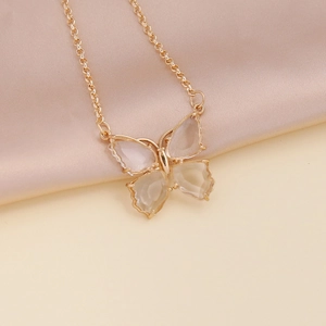 Detailed view of a gold butterfly necklace with clear wings on beige satin background