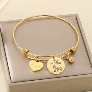 Macro shot of gold heart and round pendants with Mother's Day engravings on an adjustable bracelet