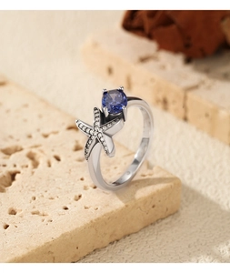Detailed view of S925 silver starfish ring with blue gemstone on travertine stone