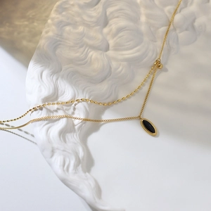 Détail du collier doré double couche avec pendentif noir ovale sur pierre en relief