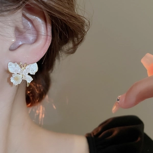 Detail of butterfly and flower stud earring with gold plating on model's ear