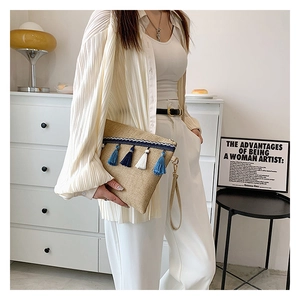 Detail of straw envelope clutch bag featuring blue and white tassels in a lifestyle setting