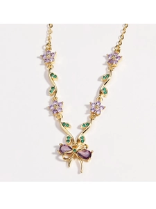 Detail einer Goldhalskette mit violetten Kristallblumen und einem Schleifenknoten-Anhänger
