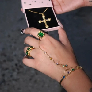 Detail of gold finger bracelet with emerald zircon and pearls on woman's hand