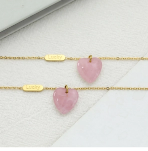 Macro detail of gold Lucky tag and pink heart pendant on stainless steel chain