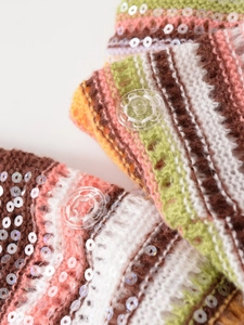 Makroaufnahme von bunt gestreiftem Strickstoff mit klaren Knöpfen und runden Pailletten