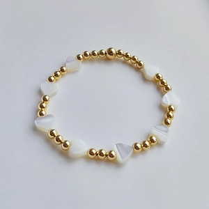 Elastic beaded heart bracelet featuring 18K gold-plated beads and white shell heart charms