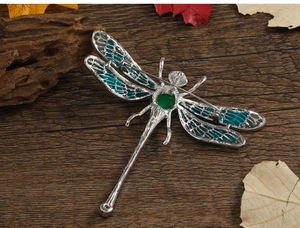 Detailed view of silver dragonfly brooch with green wings on rustic wood and dried leaves