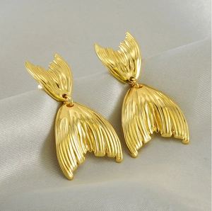 Macro shot of 18K gold fish tail stud earrings with textured finish on silk fabric