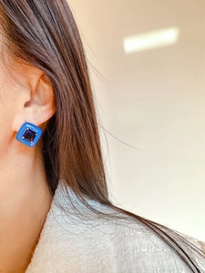 Macro shot of square light blue enamel earrings with a purple zircon stone on a model