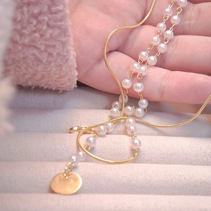 Double-layer gold snake chain and pearl necklace featuring a round gold pendant in hand