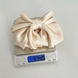 Detail view of cream satin bow hair clip on a digital scale showing weight of 37.40g