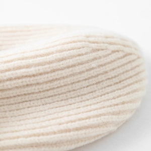 Detailed close-up of rib-knit texture on a cream winter hat showing soft yarn fibers