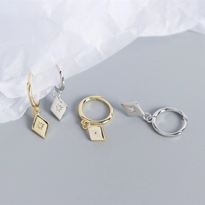 Close-up of diamond-shaped sterling silver earrings with star engraving and zircon inlay