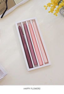 Close-up of four gradient purple to pink tapered candles on a white tabletop background