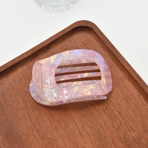 Close-up of pink acetate hair claw with iridescent pearlescent finish in a wooden tray