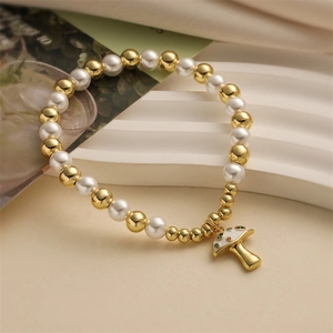 Beaded bracelet with gold beads, faux pearls and a white enamel mushroom charm on wavy base