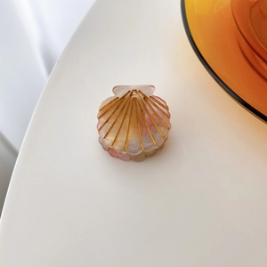 Detailed view of small seashell-shaped hair claw clip in pearlescent pink and gold