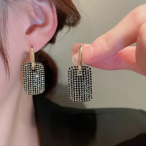 Détail macro de boucles d'oreilles créoles dorées avec pendentifs carrés en strass noirs