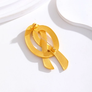 Broche nœud dorée en métal vintage avec épingle de sûreté sur socle blanc élégant
