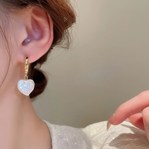 Primo piano di orecchini a cuore in perla su una modella con ganci dorati e finitura perlata