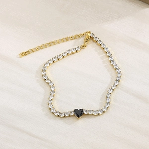 Detail of gold tennis bracelet featuring white zircons and a black heart-shaped stone