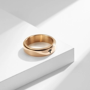 Minimalist rose gold stainless steel spinner ring featuring a black cross design on a white pedestal