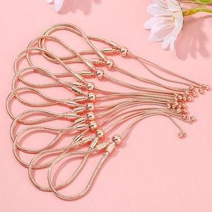 Macro shot of rose gold snake chain bracelets with adjustable beads on pink background