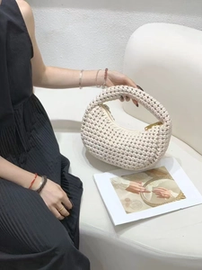 Detailed close-up of woven beige crescent bag texture with a sleek golden zipper