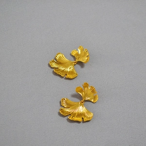 Detailed close-up of golden ginkgo leaf earrings with irregular textures on gray fabric
