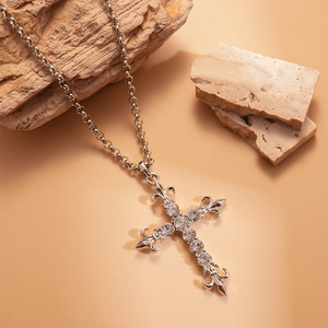 Silver fleur-de-lis cross necklace with crystal rhinestones on natural stone background