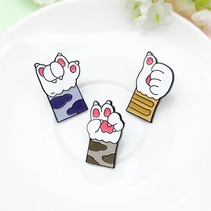 Three cute cat paw enamel pins in various colors displayed on a white ceramic plate