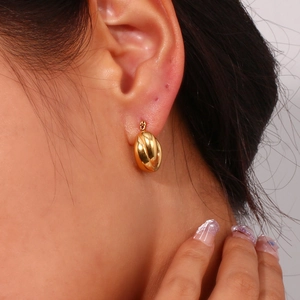 Close-up of golden grooved oval hoop earrings worn by a model in a minimalist style
