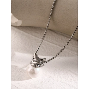 Macro view of silver bow-shaped pendant with white pearl on elegant cross chain