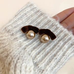 Detail of brown flocked bow earrings with champagne pearls on white knit fabric