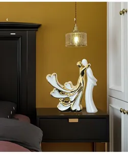Détail d'une sculpture de couple en céramique blanche et dorée sur une table de chevet
