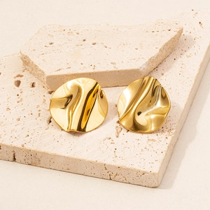 Macro detail of gold 18k plated irregular wrinkled stud earrings on a beige stone base